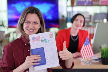 In a bright immigration office, a smiling woman proudly holds her approved visa and passport. Behind her, a staff member assists others, adding to the busy atmosphere of new beginnings.