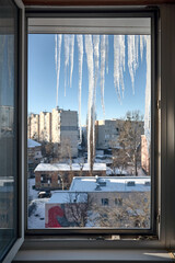 window view large icicles over defocused winter urban cityscape background