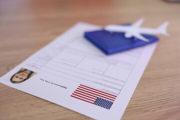 On a smooth wooden table, a passport application form is neatly arranged with a model airplane and a blue travel wallet by its side. The American flag adds a touch of patriotism.