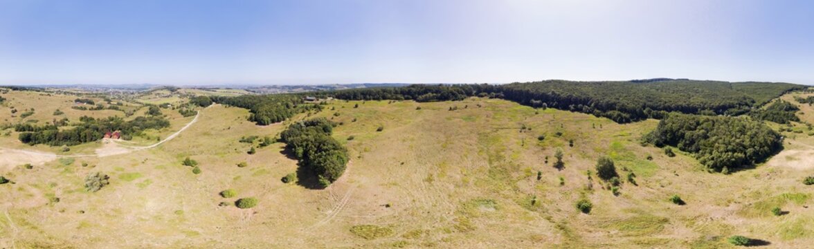 Aerial view of golden fields and emerald forests under a vast sky, a solitary house nestled amidst the rolling landscape, in 360 degrees panorama, Chernihiv Oblast, Ukraine.