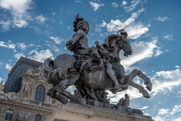 Obraz premium Paris, France - 10 11 2025: Detail view of the statue of Louis XIV and buildings of Le Louvre Museum behind