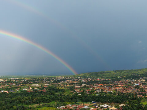 Aerial view of a vibrant rainbow arching over the sprawling landscape, casting a spectrum of light across the buildings and lush greenery, Ilesa, Osun, Nigeria.