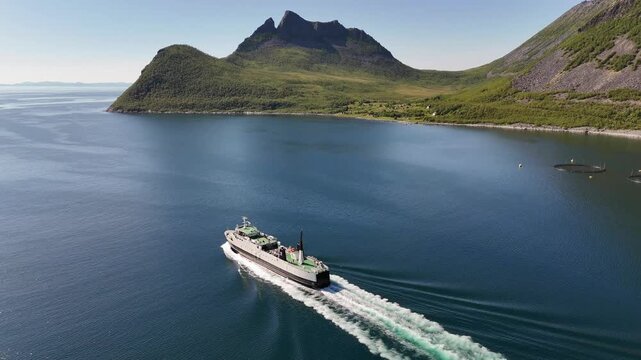 14 july 2025, Gryllefjord, Norway. Aerial, forward drone flight fjord, following ferry in fjord toward open sea, side view. Tourists on ship, tourism.  Stunning nature, arctic summer. Travelling by sh