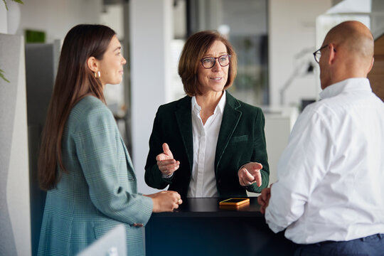 Senior businesswoman discussing with co workers near table at office