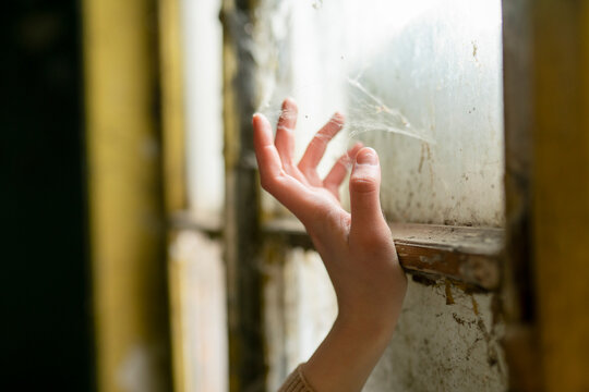 Hand touching cobweb on old window frame with green paint indoors