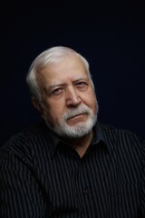 Obraz premium Older man with white beard and gray hair sits in front of plain background while looking straight ahead in a traditional setting