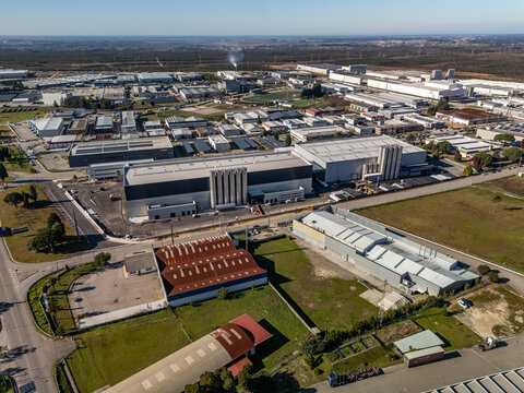 Aerial view of sprawling industrial architecture under a crisp sky, where geometric roofs meet the softer edges of green spaces, Albergaria-a-Velha, Portugal.