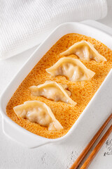 Gyoza dumplings served in creamy Tom Yum sauce with elegant minimalist presentation