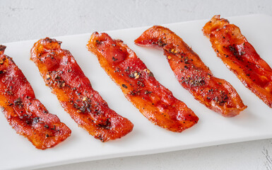 Billionaire bacon strips glazed with pepper and chili flakes on minimalist plate