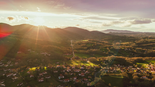 Aerial view of a golden sunset cascading over the rolling hills and quaint rooftops of a village bathed in warm, ethereal light, Ascain, Nouvelle-Aquitaine, France.