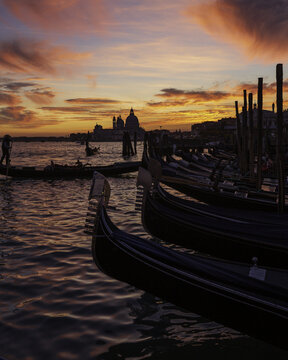View of gondolas lined up along the water's edge as the sun sets, painting the sky with vibrant hues of orange and pink, Venice, Veneto, Italy.