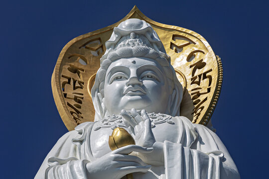 View of a pristine white statue of Guanyin in Nanshan, framed by a radiant golden halo and intricate script, against a deep azure sky, Sanya, China.