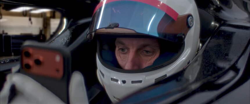 Race driver holding smartphone inside racing cockpit before start