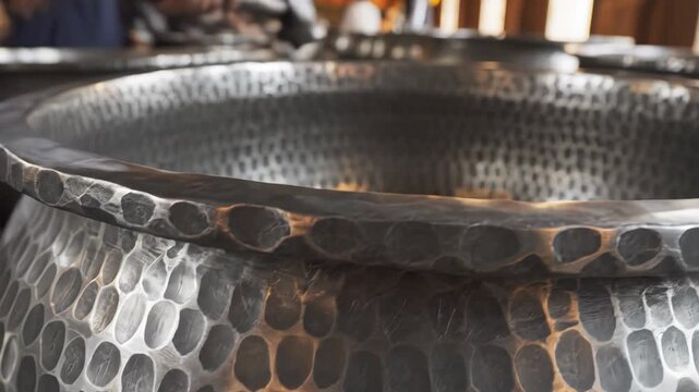 Close up of a hammered metal bowl with a textured dimpled pattern reflecting warm light creating a rustic and artisanal feel perfect for kitchenware or decorative use