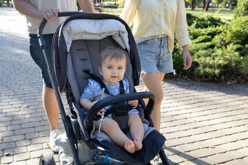 Obraz premium Parents are walking in the park with a stroller containing a sweet little baby. A family is walking along a city street on a summer day.
