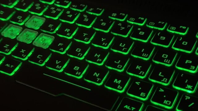 Gaming laptop keyboard close-up with green backlight and transparent WASD keys, Russian and English layout 
