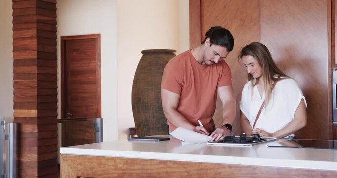 Couple in kitchen signing lease together for new apartment, smiling