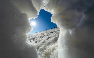 Climbers Silhouette on Snow Summit Viewed Through Natural Ice Tunnel