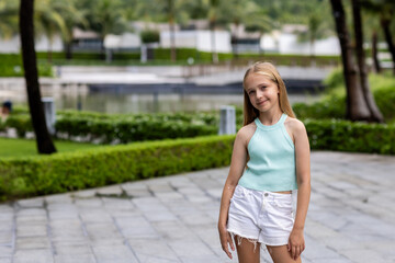 beautiful caucasian girl smiling outdoor at hot summer day. Child posing in tropical garden in...