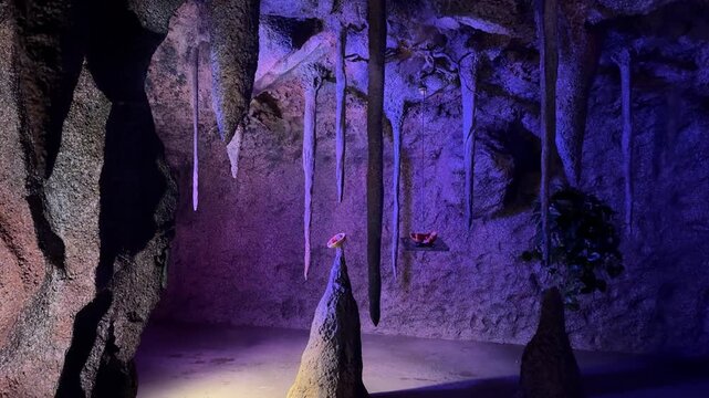 Bats flying inside limestone cave with stalactites and dramatic blue light