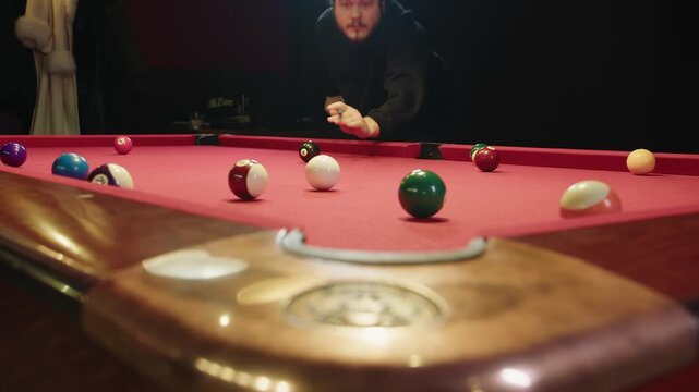 Focused caucasian adult male player lining up long bank shot on red table, male player concentrates over red felt aiming at distant pocket with cinematic low angle composition and scattered balls