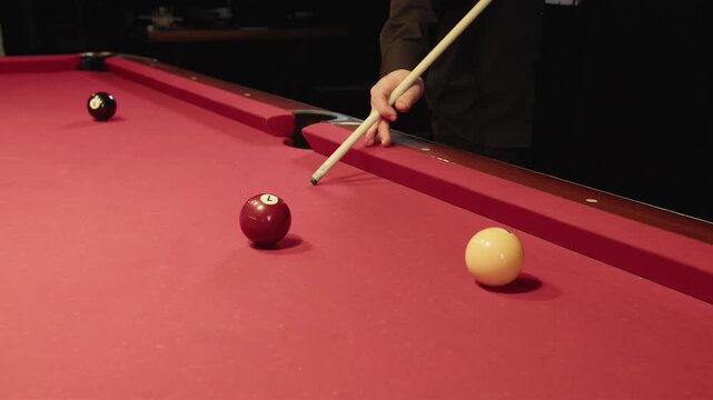 Precision shot from edge moves balls across red felt table, male player executes calculated hit by cue as balls roll in cozy billiard room, strategic play with friendly competitors.