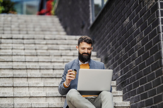 Portrait of a businessman sitting on staircase with coffee to go and laptop at downtown district and working on a project.