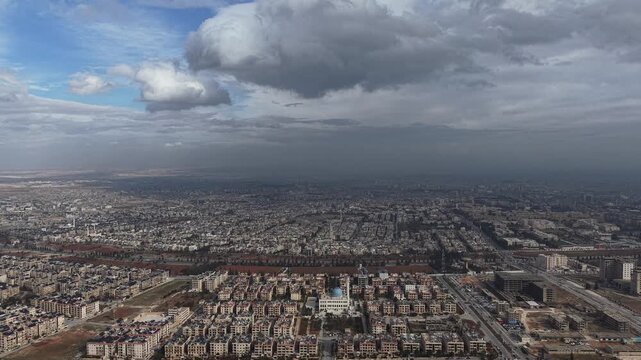 In Aleppo, Syria breathtaking aerial drone footage captures the urban skyline of the city under a dramatic sky. The video features high-angle views of residential neighborhoods and architecture, showc