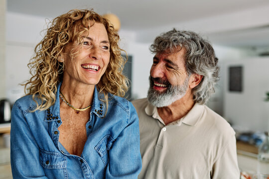 Portrait of happy senior mid aged mature couple prepering meal and having fun dancing and embracing in kitchen at hpme