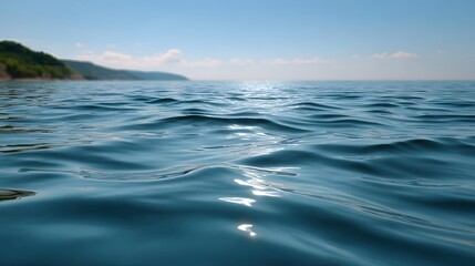 Obraz premium Sunlit ocean ripples with a blurred green coastline under a clear blue sky