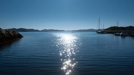Obraz premium Serene bay with sparkling sunlight reflections on calm blue water sailboats docked in a marina under a clear sky