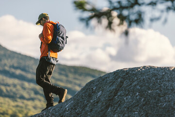 African American man hiking down a mountain with a backpack in an orange coat with ski area trails off in the distance in Vermont, New England, USA. © Justin