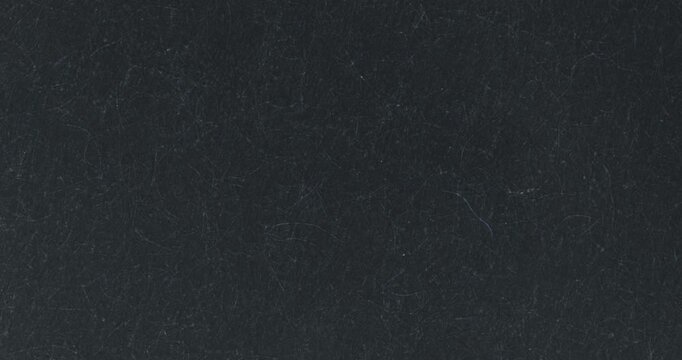 Stop-motion video of dark felt-like textile surface with subtle diagonal ridges and scattered lint fibers. Moody abstract background for minimal, craft, fashion, and design use.