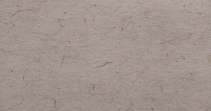 Stop-motion style close-up of beige recycled paper surface with visible fibers and tiny colored specks. Natural handmade texture for eco design, overlays, or backgrounds.