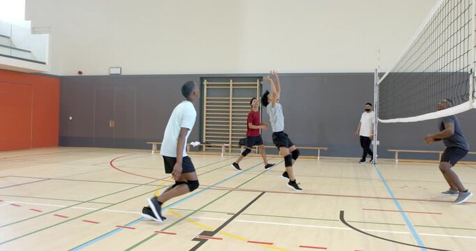 African American man spiking volleyball to return opponent serve after setter lifting ball in gym