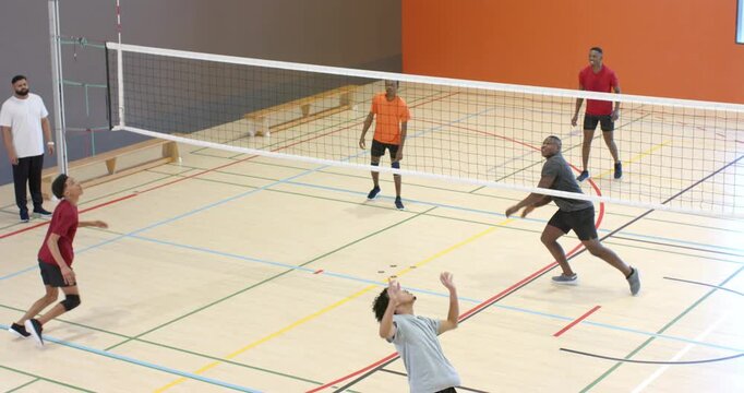 Adult male setter tracking lobbed ball performing set by net on court for red-shirt attacker