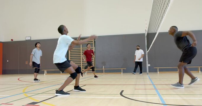 African American man reacting to set in gym, jumping and spiking volleyball while blocker jumping