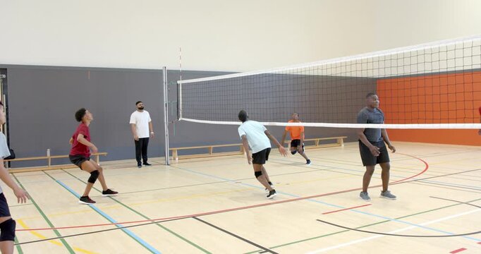 Diverse male players receiving serve over net blocking spiking digging and shifting on gym court