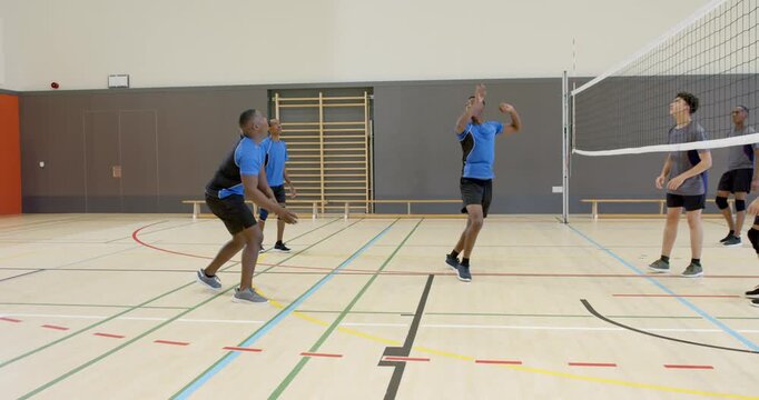 Diverse male volleyball players on receiving serve bumping then spiking ball over net in school gym