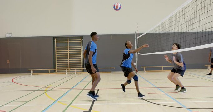 African American male in jersey bumping, placing pass over volleyball net to return ball in gym