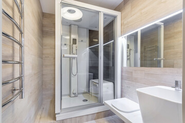 A shower area features a glass enclosure and a modern design. The bathroom has light wood walls and...