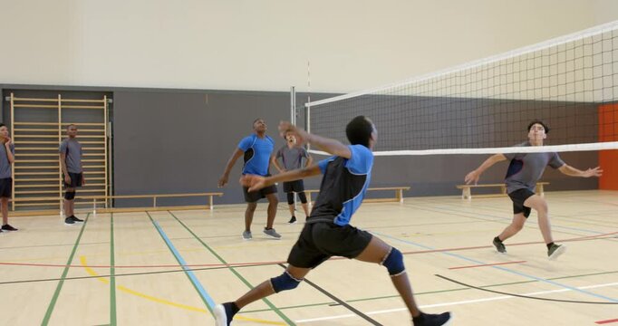 After setter raising ball, male volleyball player jumping, spiking over net at gym during rally