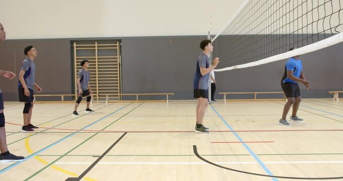 Asian male in grey jersey blocking, spiking after opponent serving on school gym court, copy space
