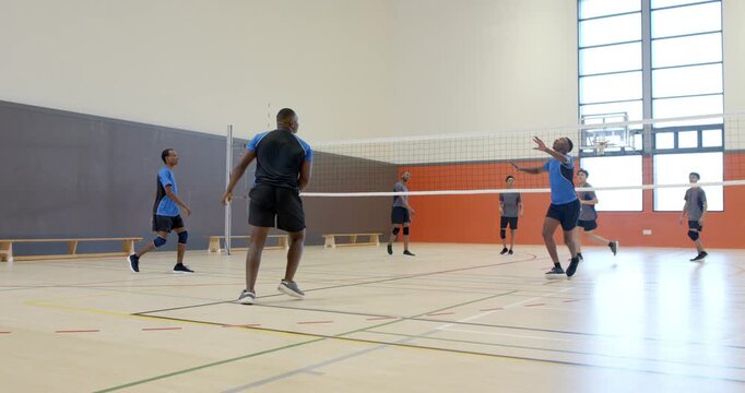 Diverse male teams volleying, blocking, regrouping at net after gray serve for point in school gym