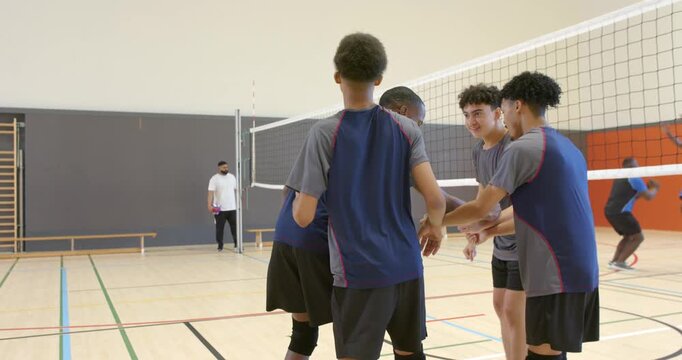 Diverse team in jerseys sharing pep talk near net, walking to spots after referee raising ball