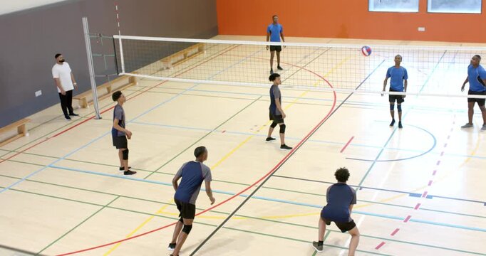 Team B tossing ball on court with referee monitoring net causing navy-blue player diving to dig
