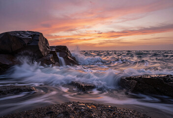 Dramatic sunset waves crashing against rugged coastal rocks