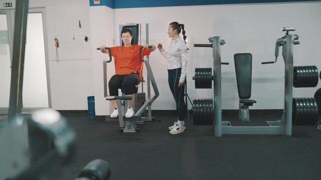 Personal fitness trainer assisting woman exercising on pec deck machine