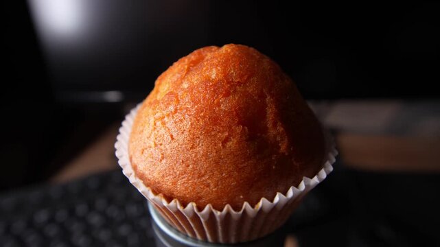 A close-up shot of a golden-brown muffin in a white paper wrapper, highlighting its perfectly domed top and slightly crisp texture. 