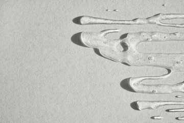 Clear cosmetic gel spreading on textured gray background, showing light and shadow